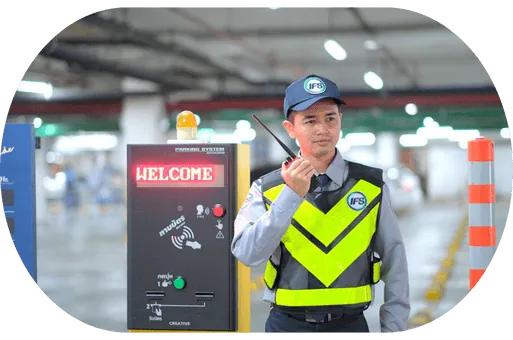 เจ้าหน้าที่รักษาความปลอดภัย IFS ประจำจุดทางเข้าอาคารหรือที่จอดรถ สวมเสื้อกั๊กสะท้อนแสงและสื่อสารผ่านวิทยุ เพื่อควบคุมการเข้า-ออกและดูแลความปลอดภัย
