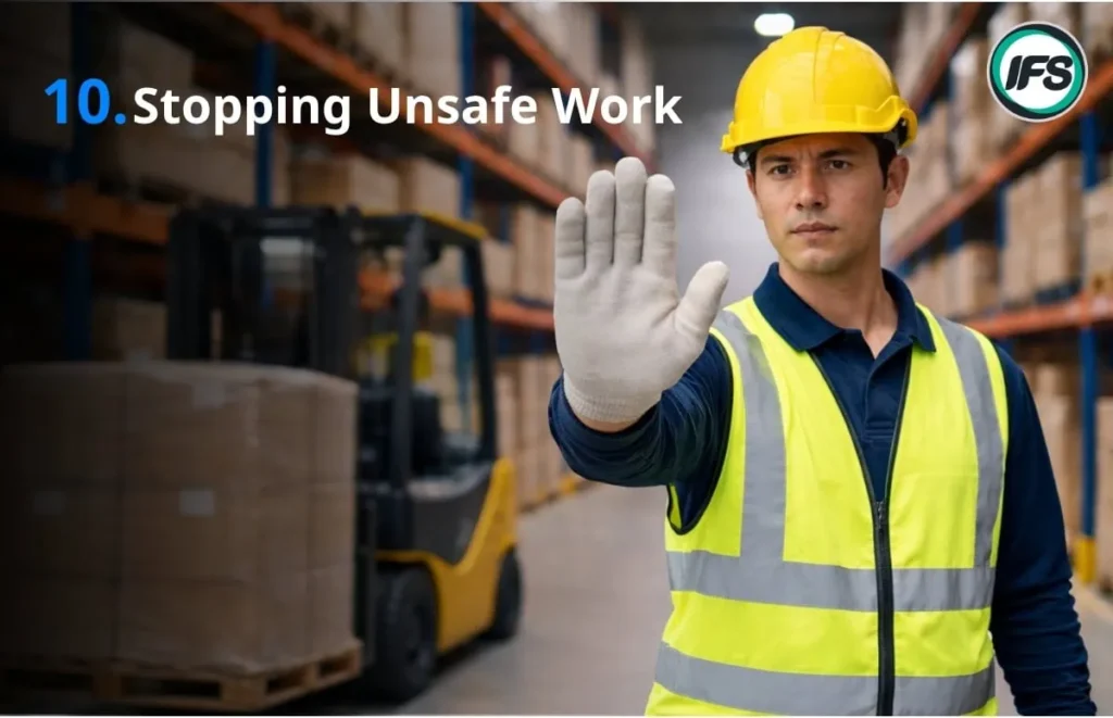 พนักงานคลังสินค้าสวมหมวกนิรภัยและเสื้อสะท้อนแสง ยกมือเป็นสัญญาณหยุดเพื่อป้องกันการทำงานที่ไม่ปลอดภัย ใกล้รถโฟล์คลิฟท์ในโกดัง - ภาพประกอบบทความ 10 กฎความปลอดภัยของกลุ่มบริษัท ไอเอฟเอส ฟาซิลิตี้ จำกัด
